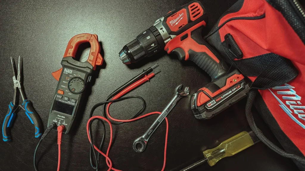 Pliers, a clamp meter, a wrench, a screwdriver and a drill laid out on a dark work surface