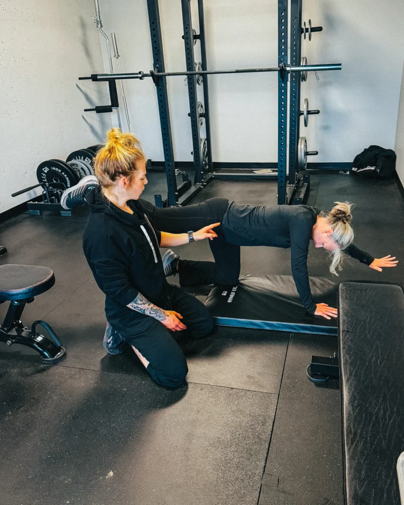 Nina kneeling beside a client on a mat, adjusting their position mid-exercise